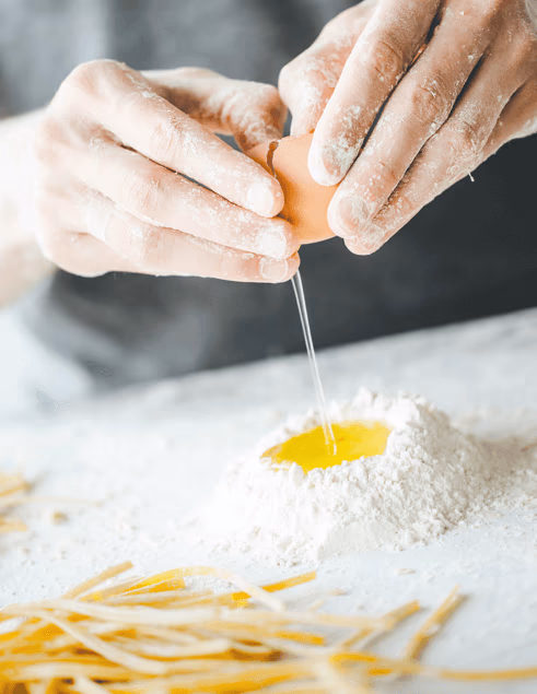Hände bei der Pasta-Herstellung – Ei wird in frisches Mehl aufgeschlagen